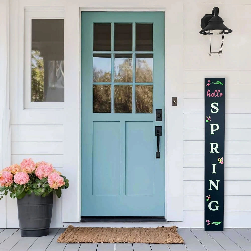 A spring welcome sign that says &quot;hello spring&quot; next to a blue farmhouse front door crafted with a porch chalkboard using magnetic large letter stencils, flower and butterfly spring stencils and erasable painting pens to make a DIY sign